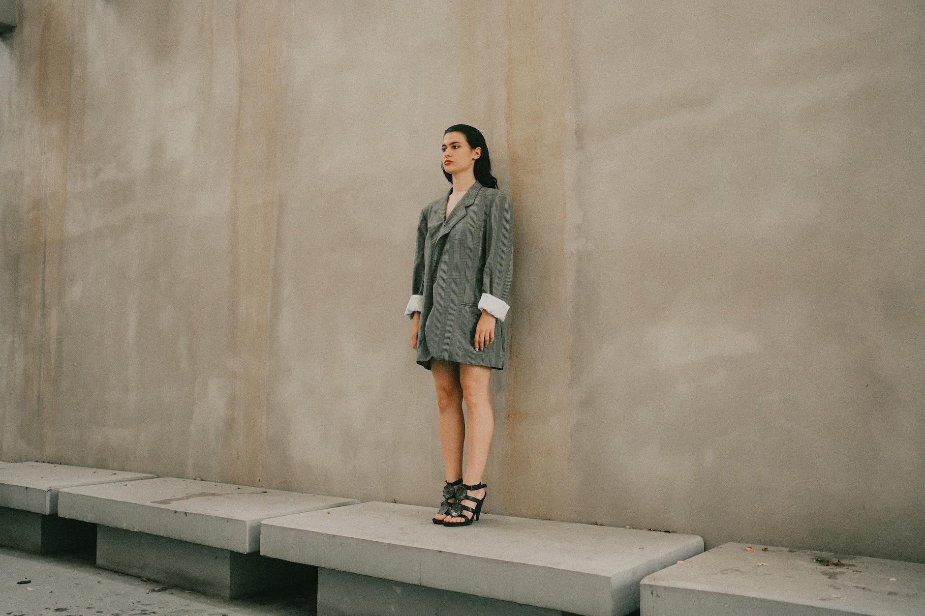 Kobieta w oversize’owej marynarce stoi przy betonowej ścianie